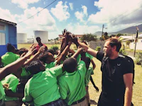 a man in green shirts giving a high five to a group of children