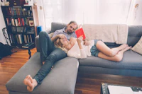 a man and woman laying on a couch reading a book