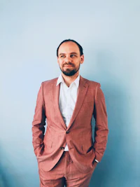 a man in a pink suit standing against a blue wall